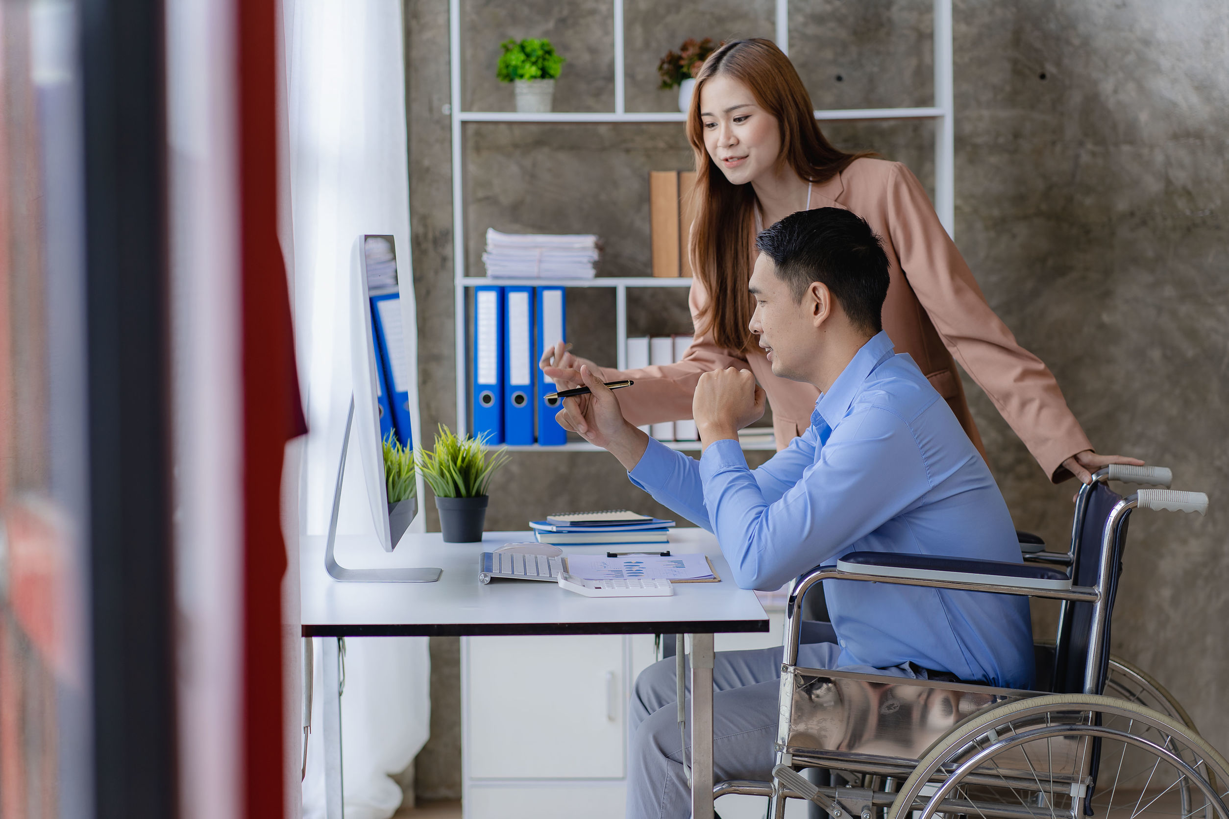 一名僱主站在一名坐輪椅的員工旁商討工作。